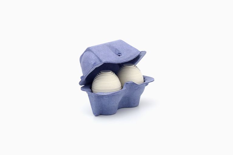 Limited edition print of two layered white cardboard eggs in a deep blue two-egg paper pulp carton